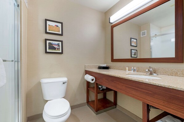 A bathroom with a toilet, sink, mirror, and framed pictures on the wall.