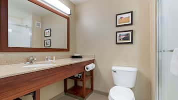 A bathroom with a wooden vanity, a large mirror, a toilet, and framed pictures on the wall.
