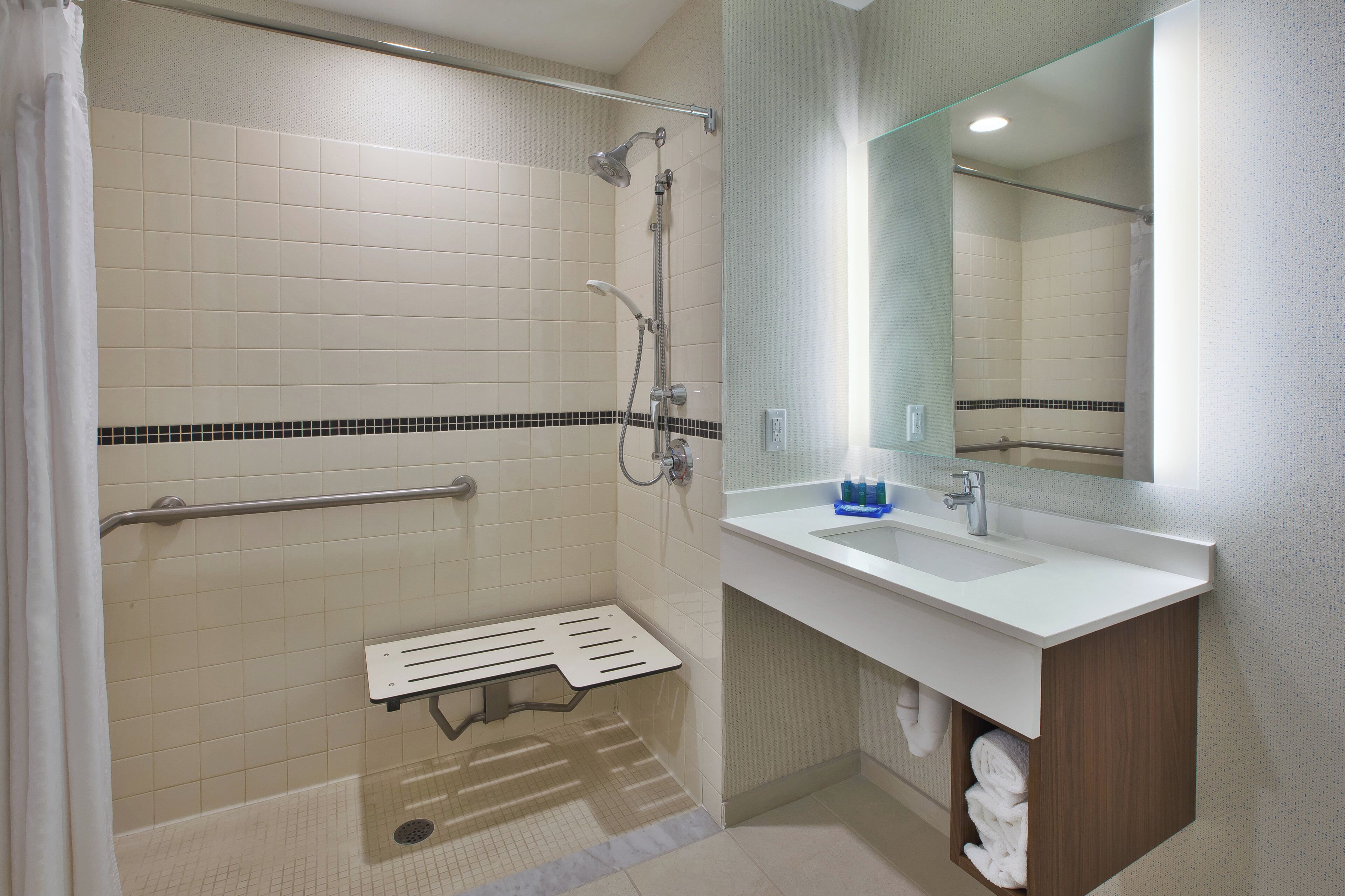 A bathroom with a shower, a sink, a mirror, and a towel rack.