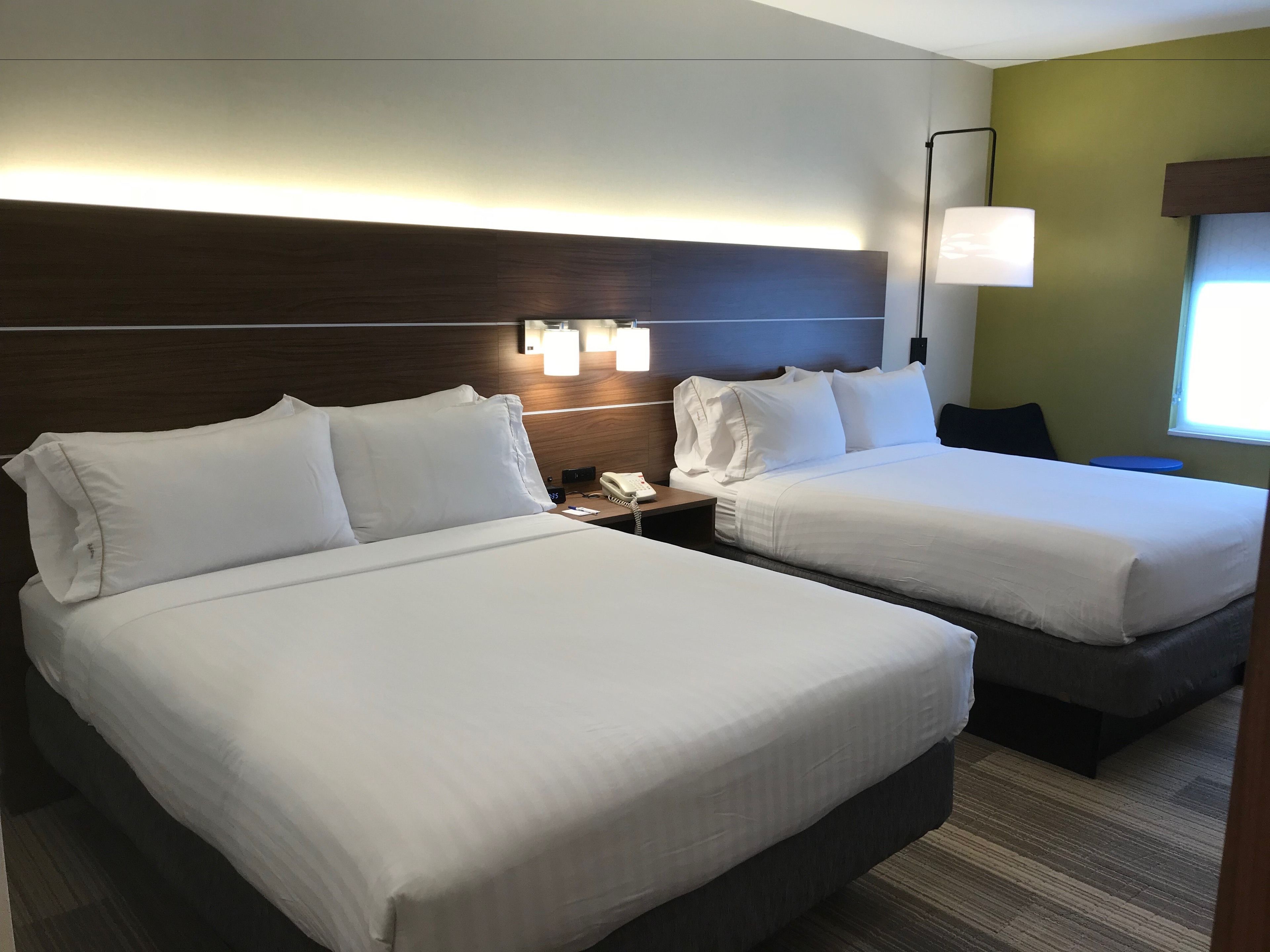 A hotel room with two beds, a nightstand, a lamp, and a window with a view.