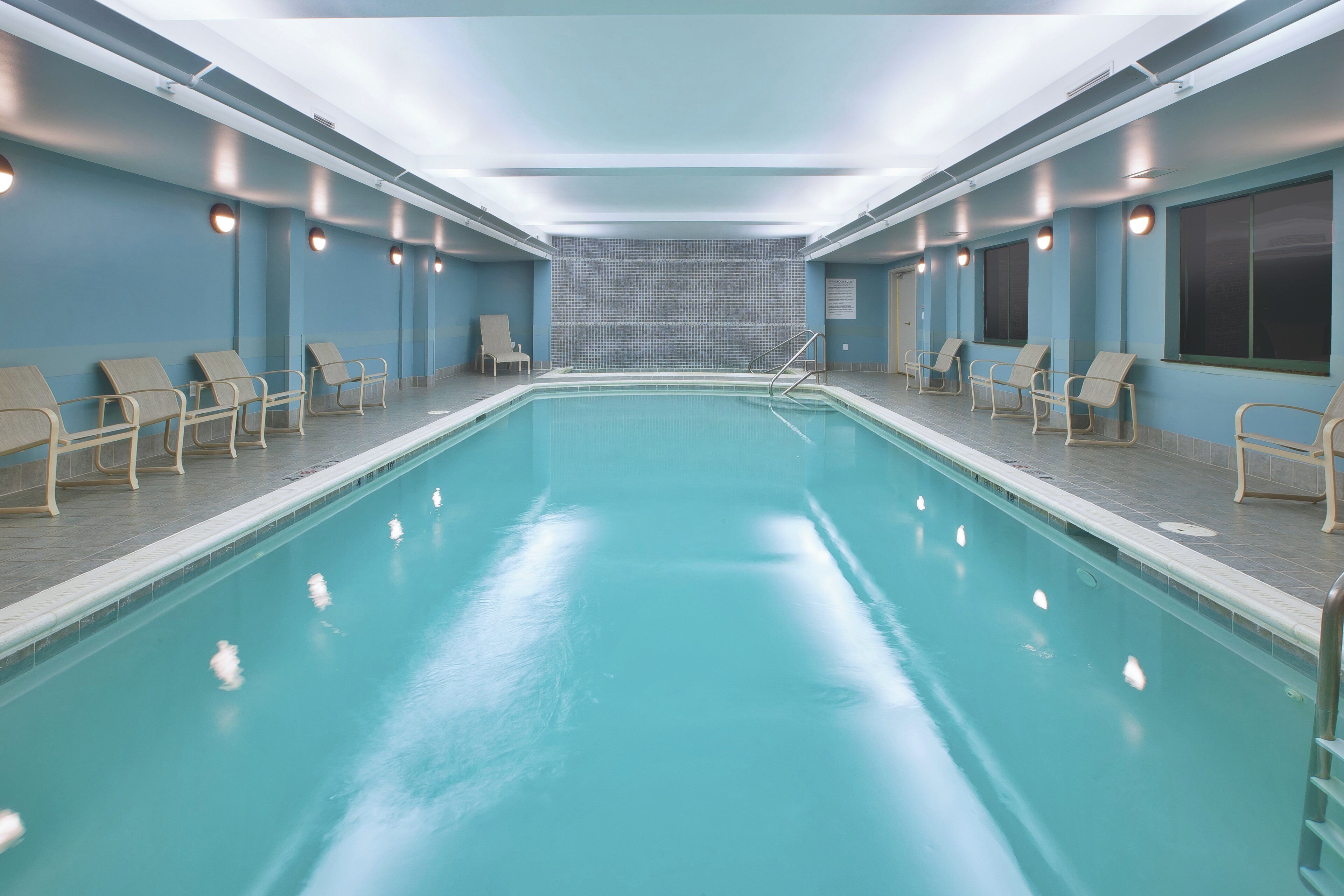 Ein großer, überdachter Pool mit mehreren Liegestühlen und einer gefliesten Wand im Hintergrund.