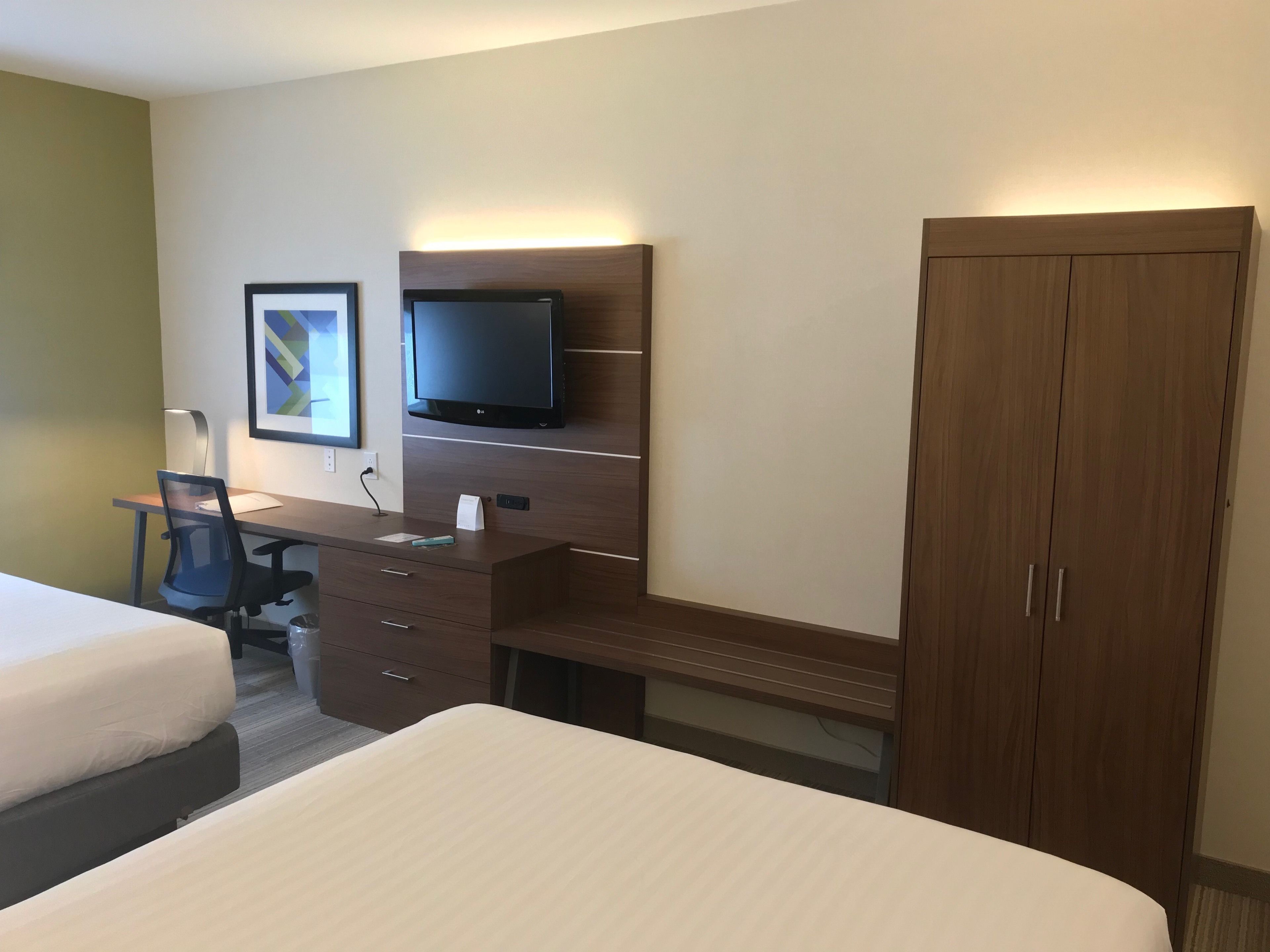 A hotel room with a bed, a desk with a chair, a television, and a wardrobe.