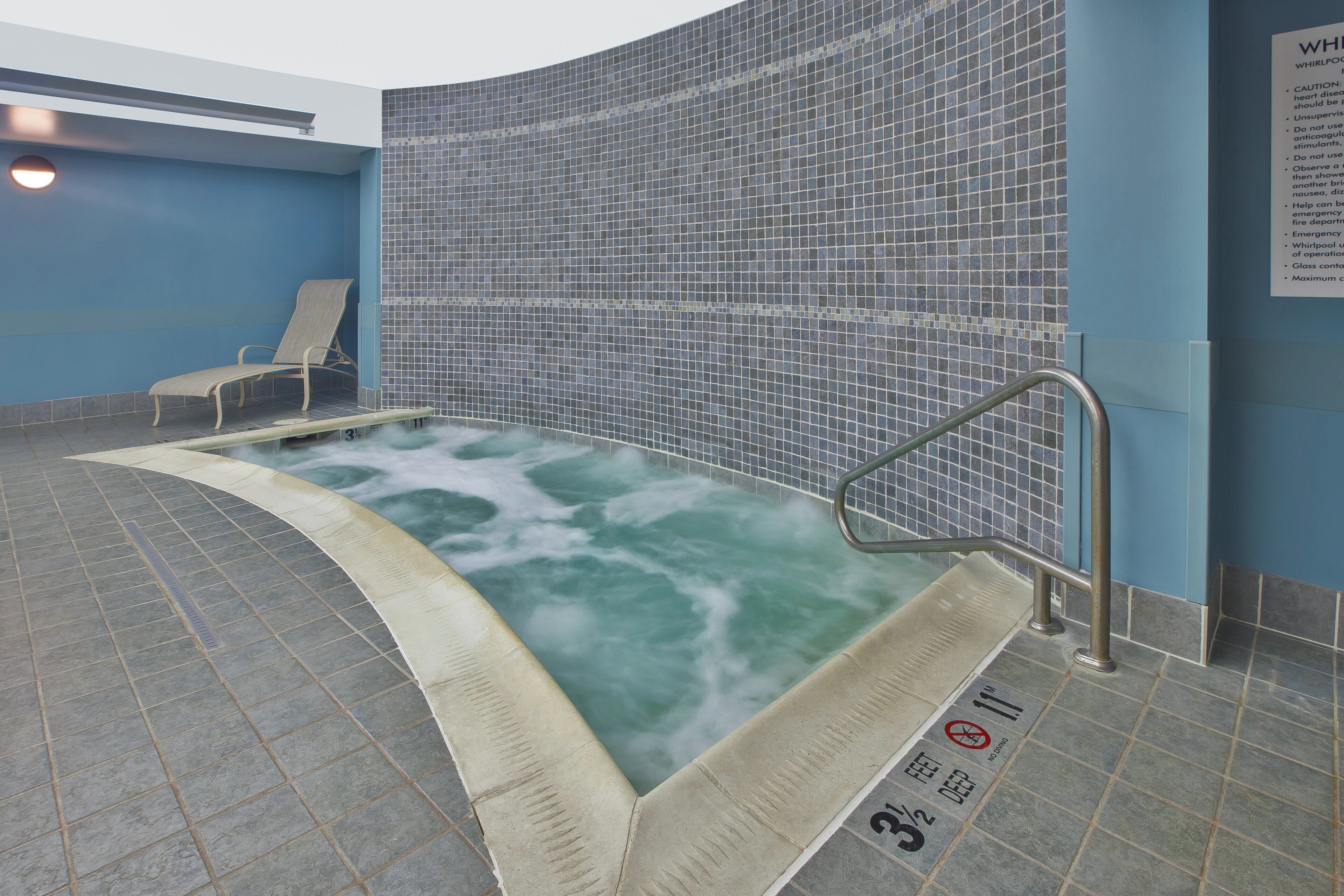 A whirlpool with a tiled wall, a bench, and a safety sign.