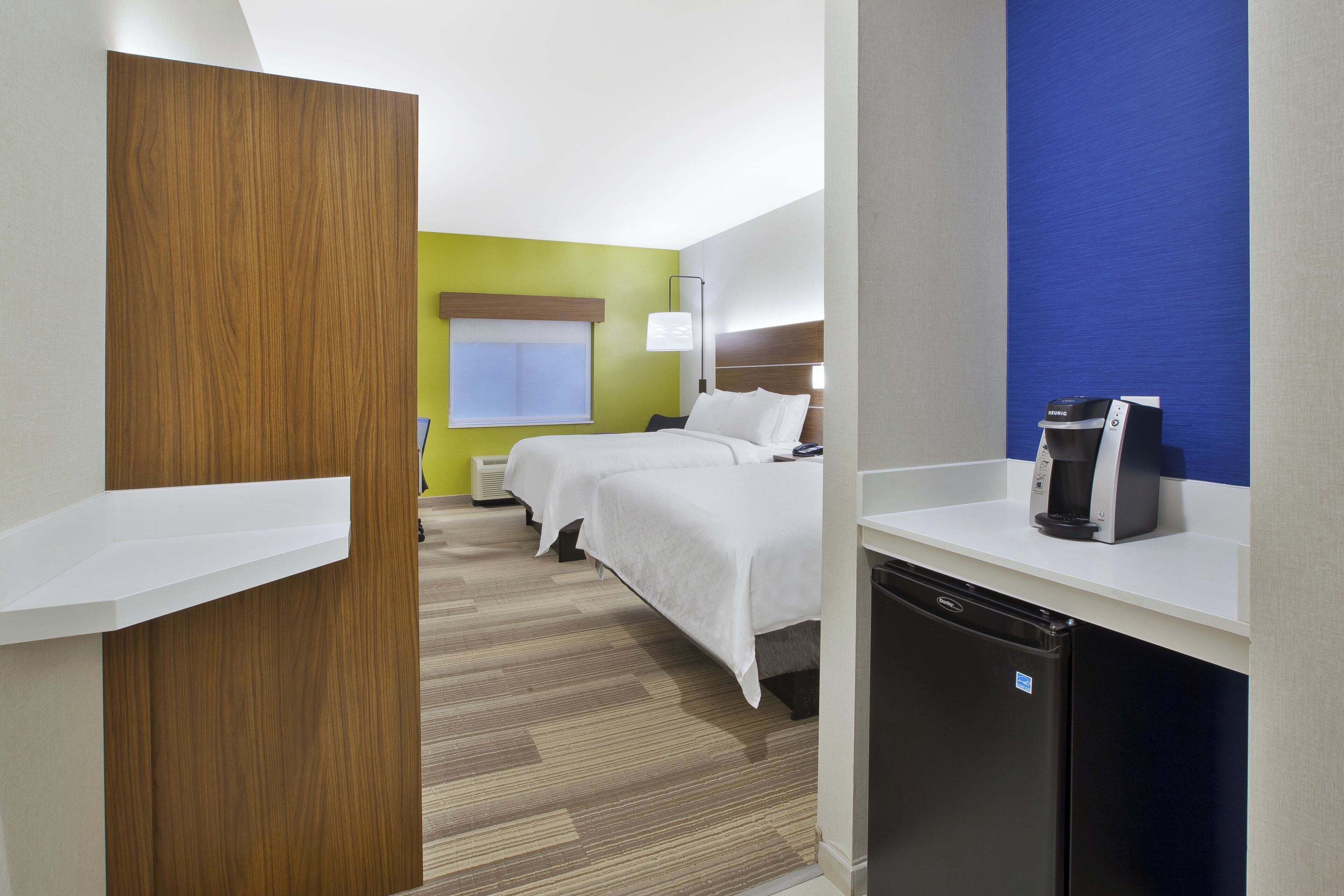 Una habitación de hotel con una cama, cafetera, escritorio y un refrigerador pequeño.