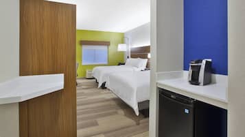 Una habitación de hotel con una cama, cafetera, escritorio y un refrigerador pequeño.