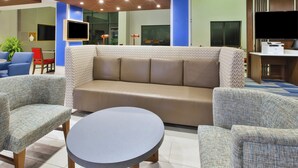 A modern hotel lobby with a sofa, chairs, a round table, and a flat-screen TV.