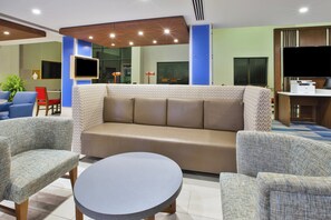 A modern hotel lobby with a sofa, chairs, a round table, and a flat-screen TV.