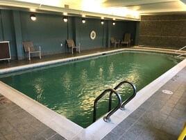 Una piscina interior con suelo de baldosas, una escalera de piscina y varias sillas de descanso a lo largo de la pared.