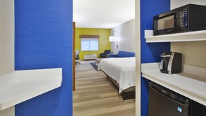 A hotel room with a bed, a desk, a microwave, a coffee maker, and a refrigerator.