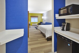 Una habitación de hotel con cama, escritorio, microondas, cafetera y refrigerador.