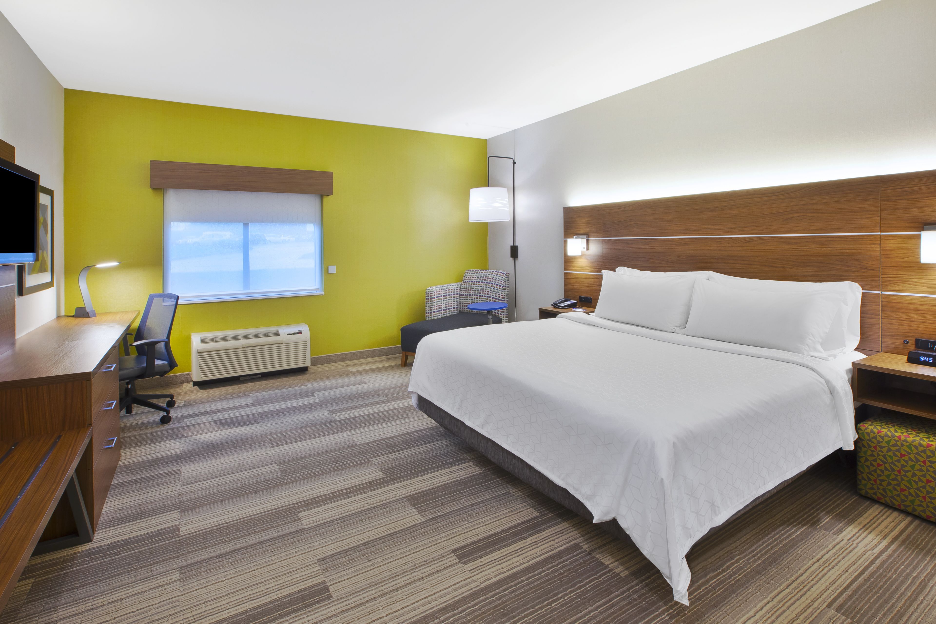 Une chambre d’hôtel avec un lit, un bureau, une chaise et une fenêtre avec des stores.