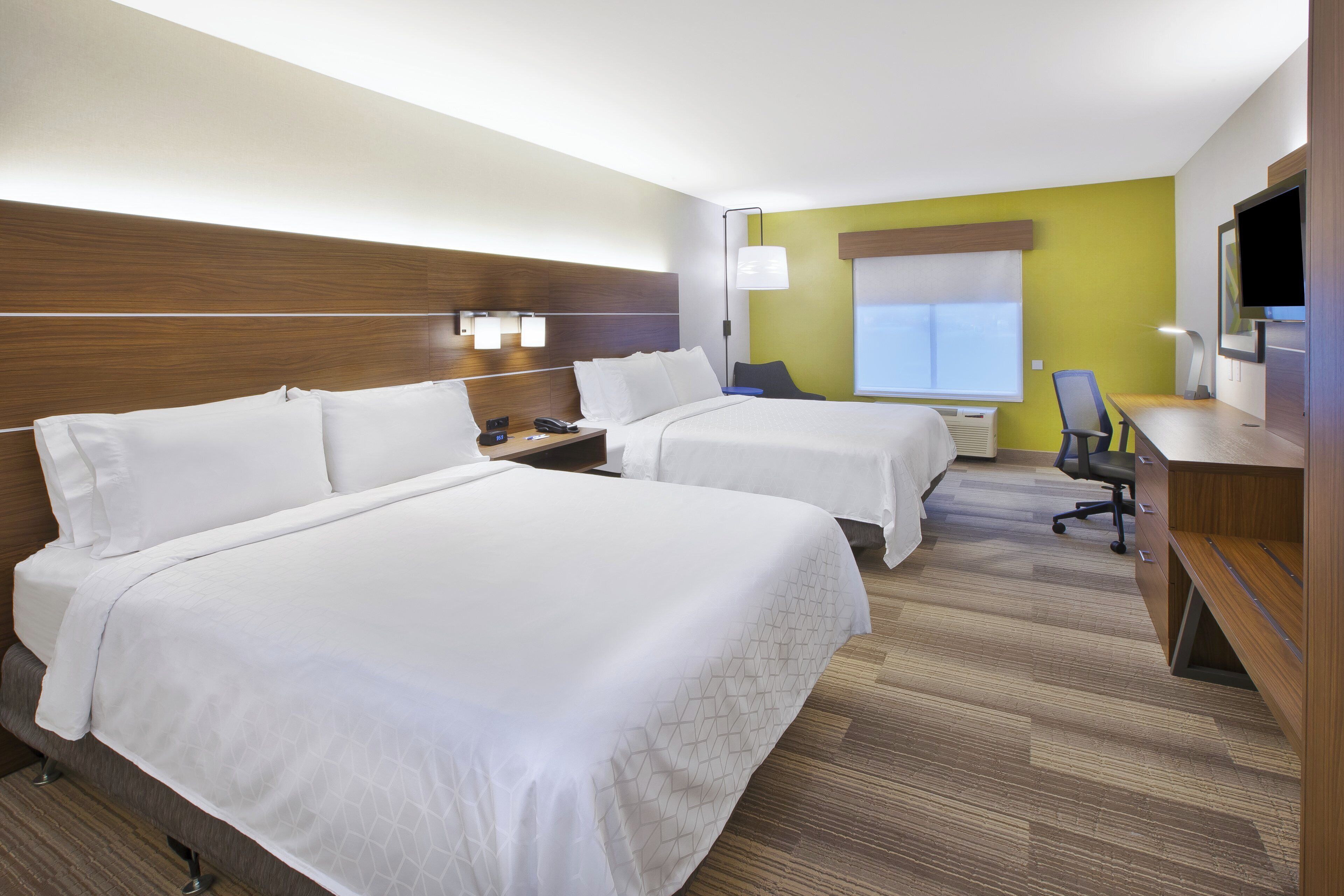 A hotel room with two beds, a desk, a chair, a TV, and a window.