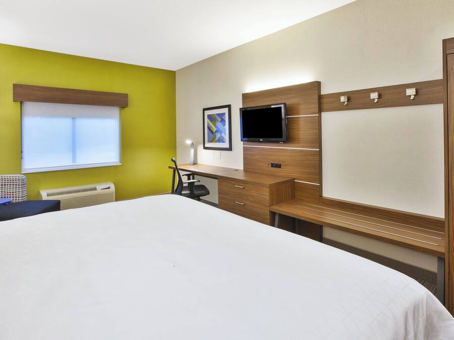 A hotel room with a bed, desk, chair, TV, and a window.