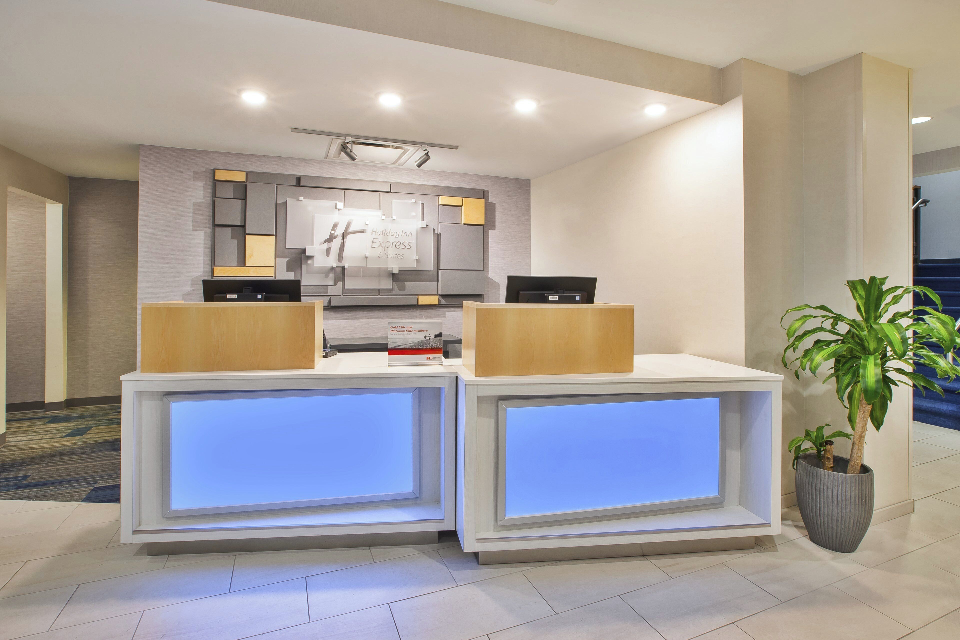 A reception desk with a digital display, a wall-mounted sign, and a potted plant.
