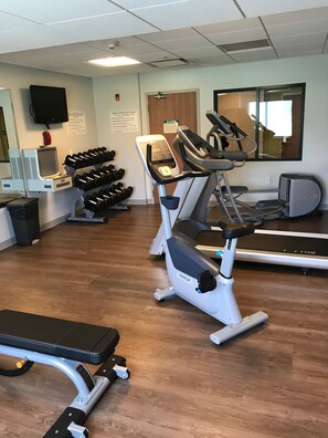 A gym with exercise equipment, including treadmills and an elliptical, and a wall-mounted TV. - Holiday Inn Express Hotel & Suites Rochester - Victor by IHG (Victor)