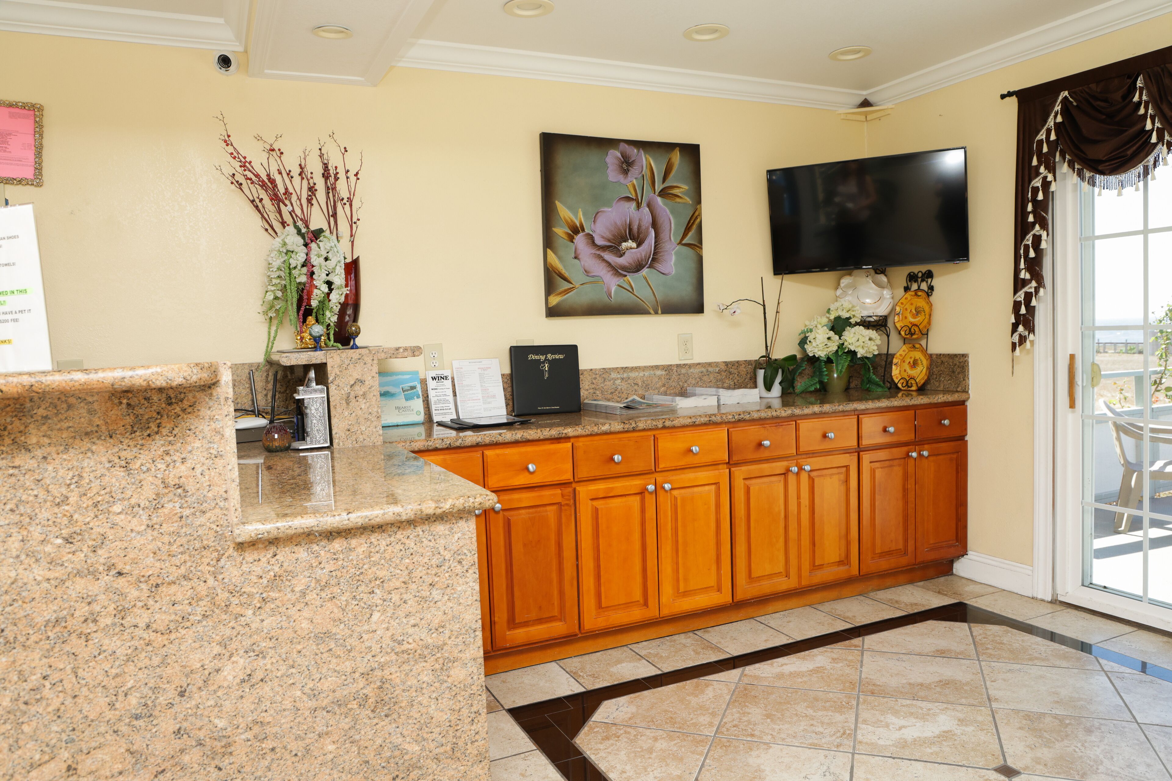 A kitchen with granite countertops, wooden cabinets, a flat-screen TV, and a large window with a view.