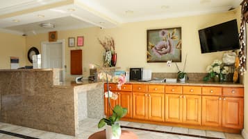 A hotel reception area with a granite counter, wooden cabinets, a television, and a painting of flowers on the wall.