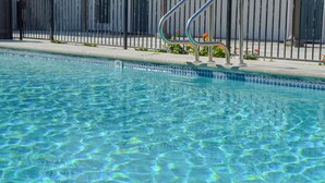 A clear swimming pool with a metal ladder and a metal railing.