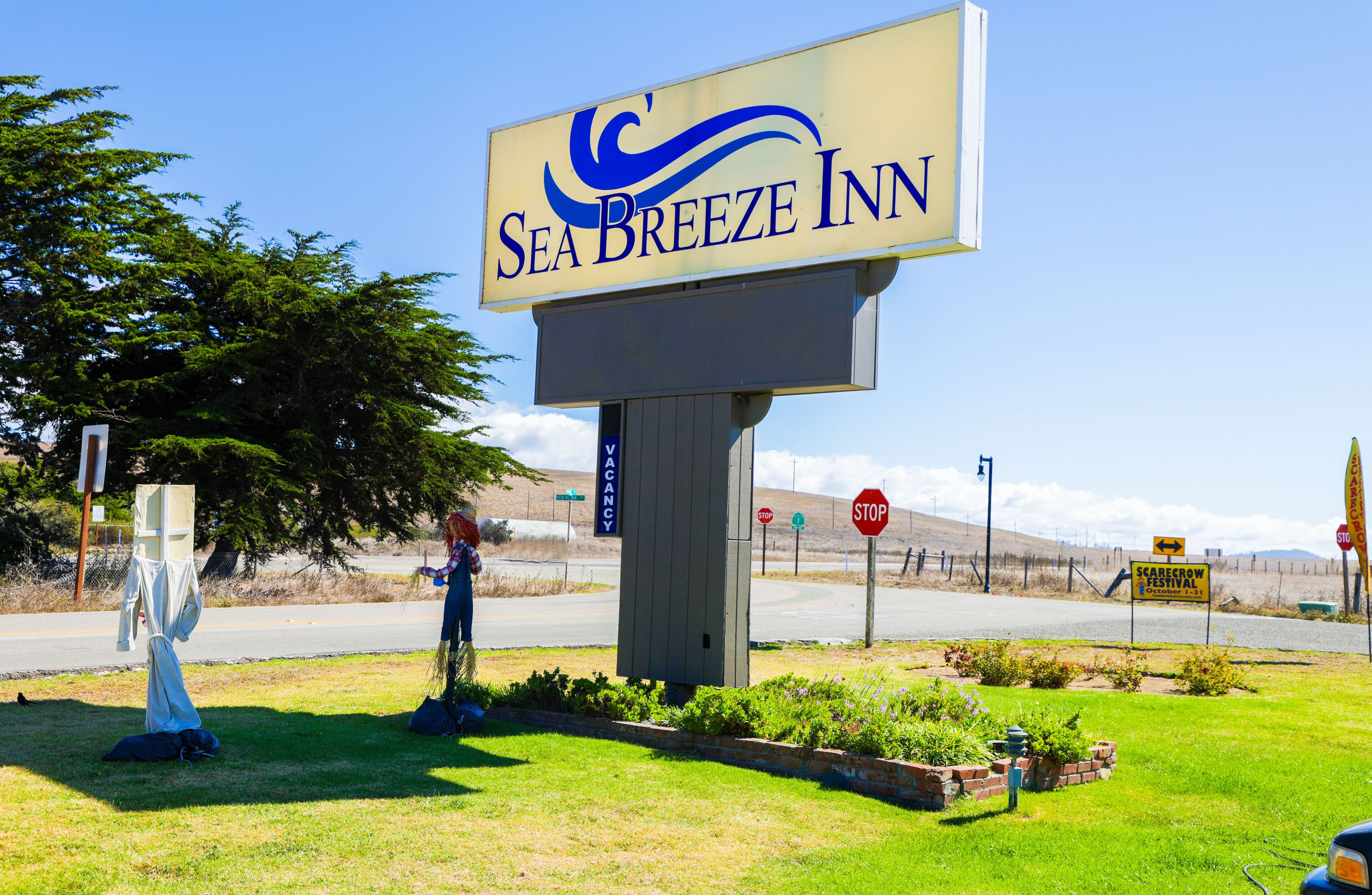 A sign for Sea Breeze Inn with a clear view of the surrounding area including a road, a stop sign, and a Scarecrow Festival sign.