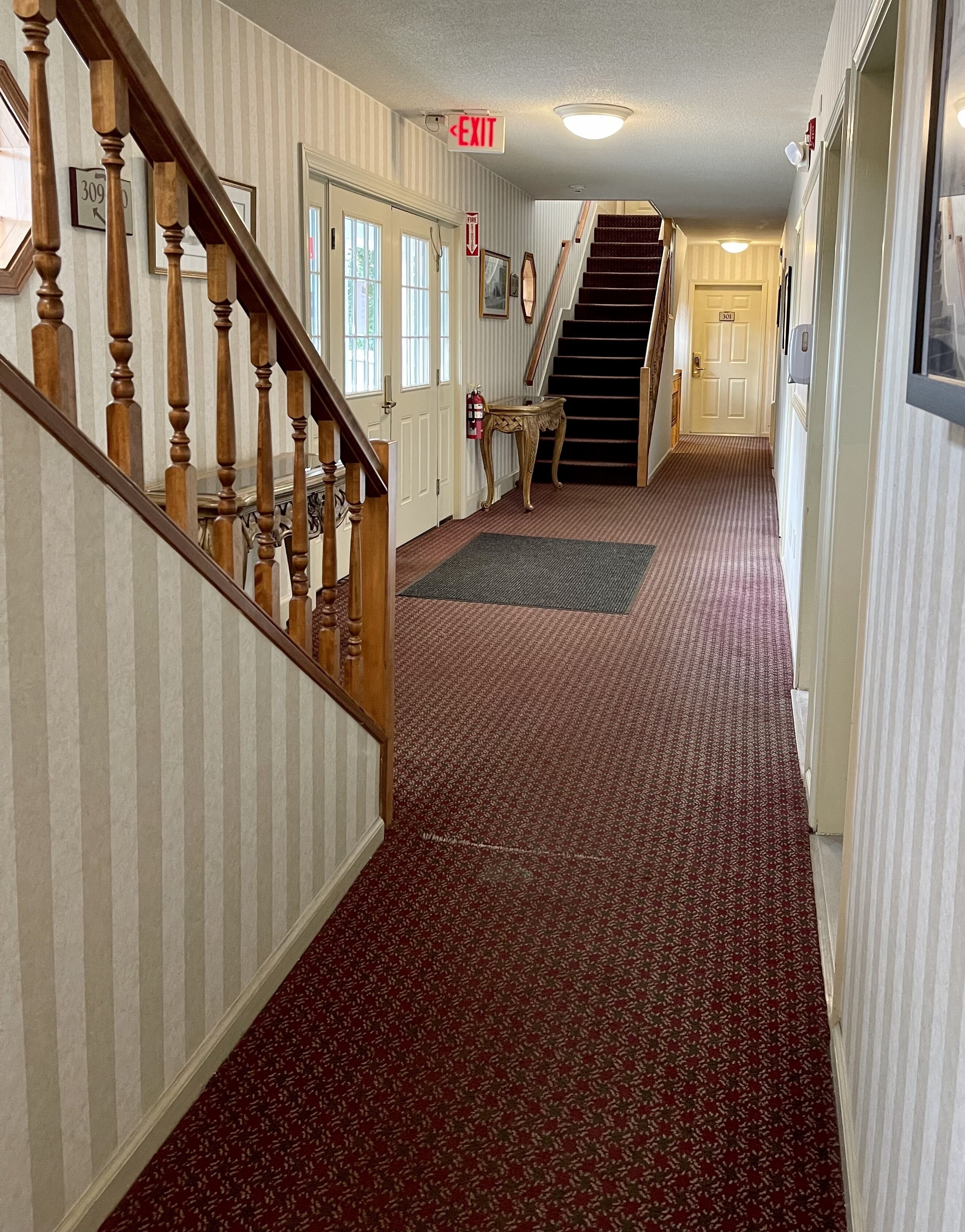 A hallway with a carpeted floor, a wooden staircase, and a door marked '309'.