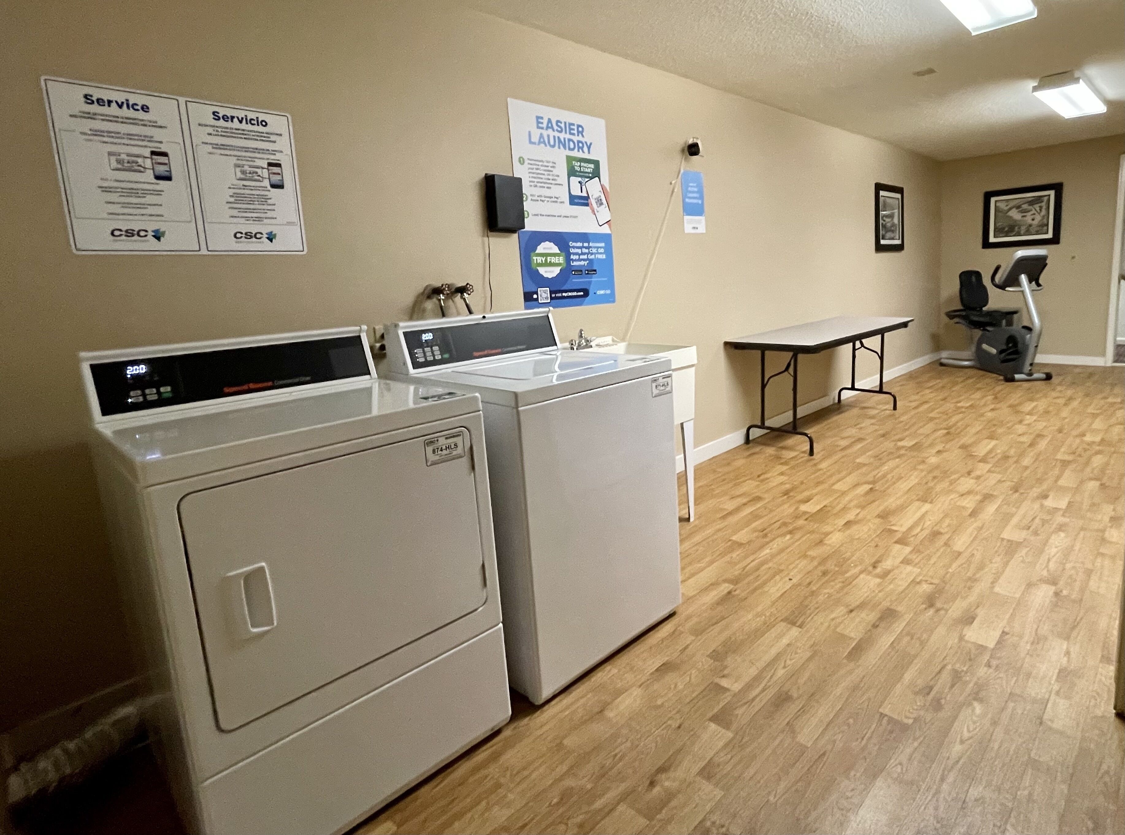 A laundry area with two front-loading washers and dryers, a table, and a treadmill.