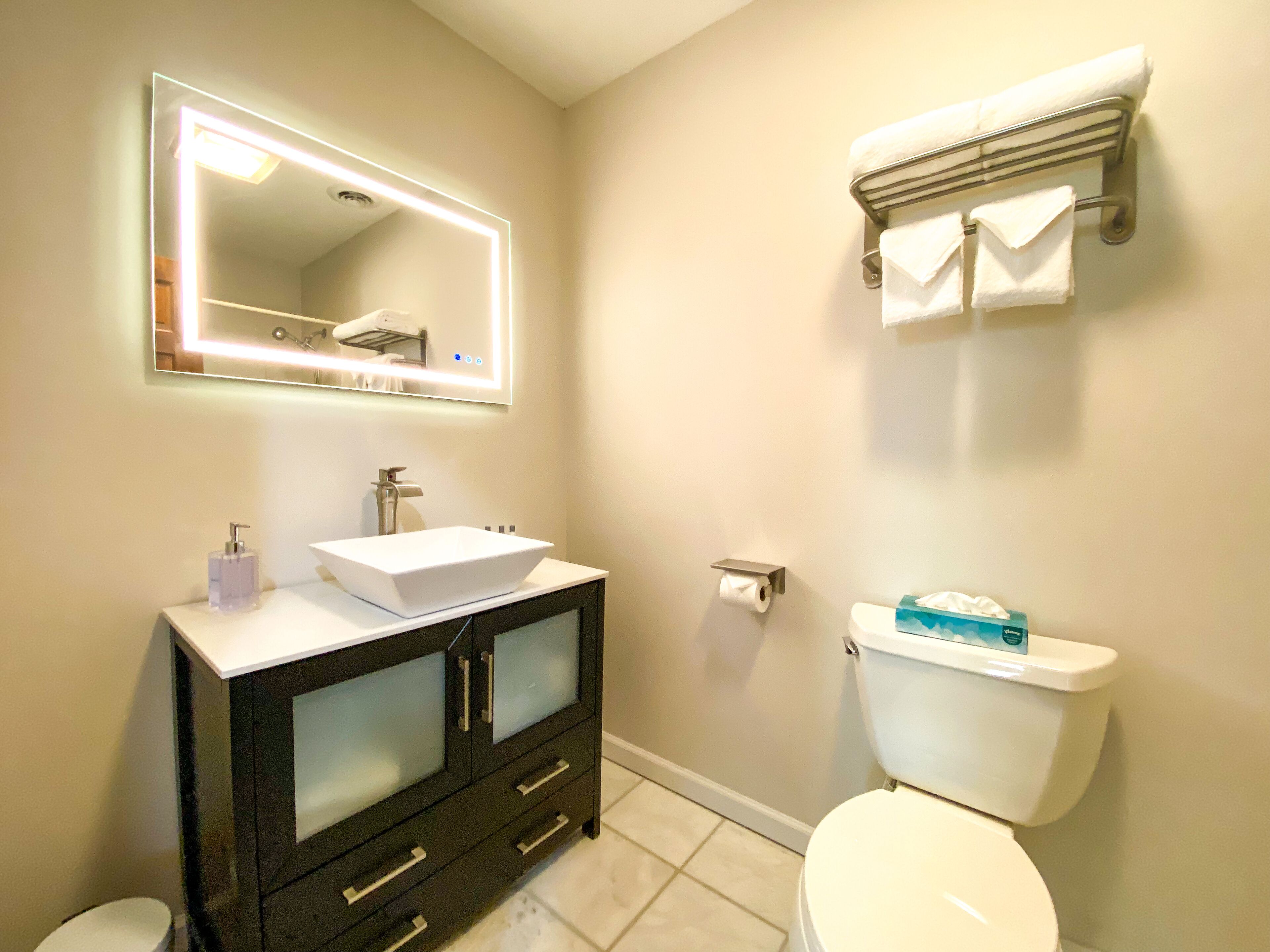 A bathroom with a white sink, a mirror with lights, a toilet, and a towel rack.
