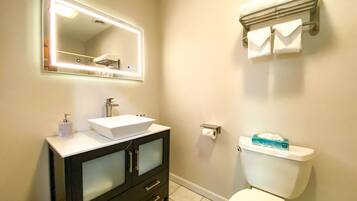 A bathroom with a white sink, a mirror with lights, a toilet, and a towel rack.