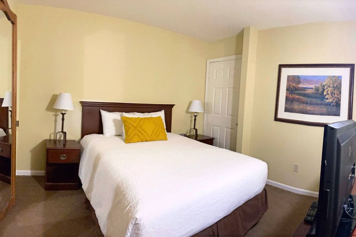 A hotel room with a large bed, two bedside tables with lamps, a wooden wardrobe, a door, and a framed picture on the wall.