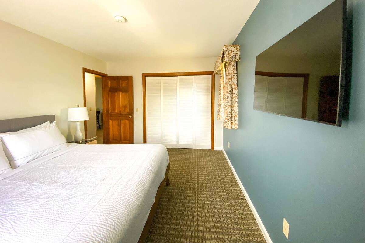 A hotel room with a bed, a nightstand, a lamp, a wardrobe, and a television mounted on the wall.