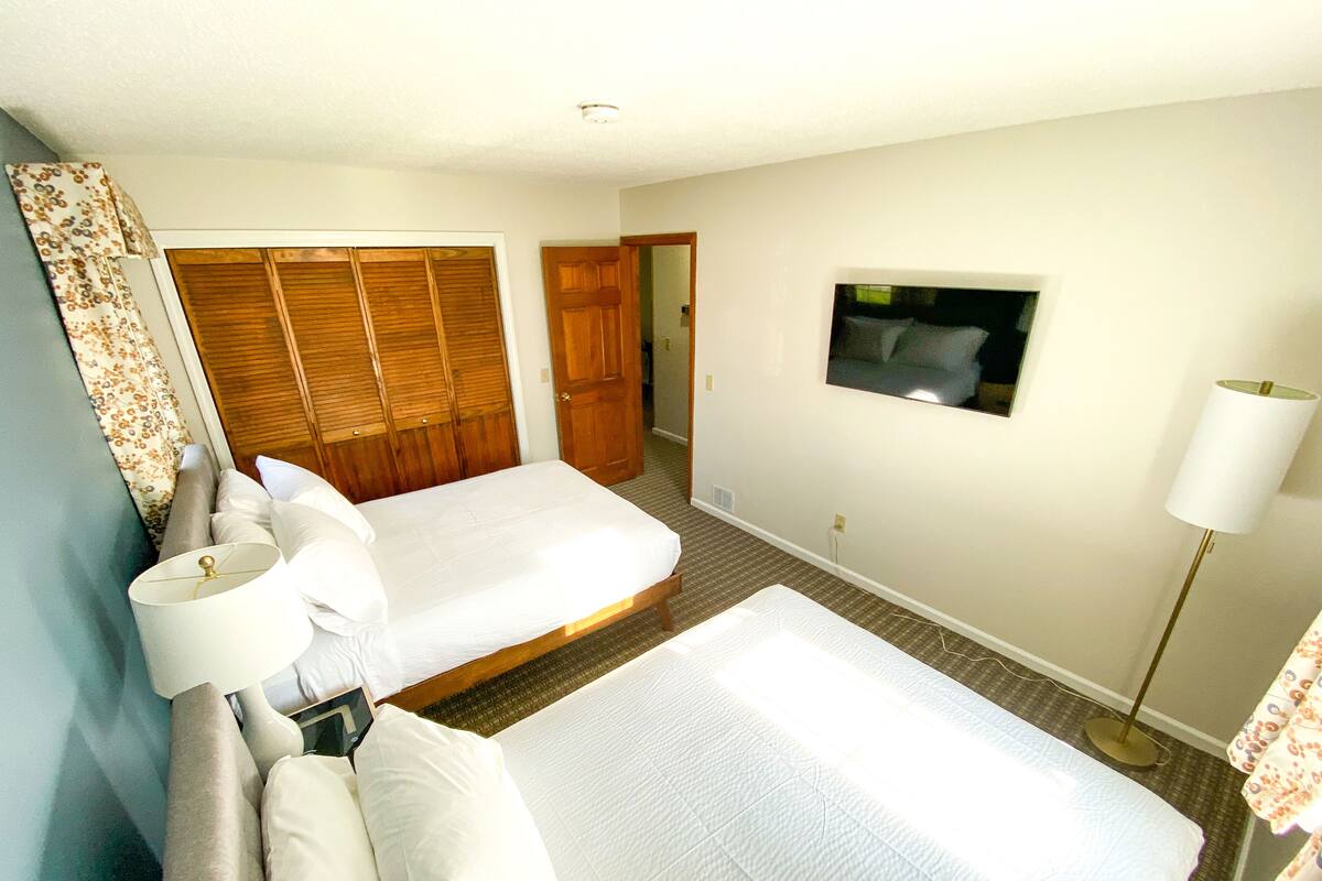 A hotel room with two beds, a TV mounted on the wall, a bedside lamp, and a wooden wardrobe.
