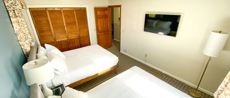 Habitación de hotel con dos camas, televisión montada en la pared, lámpara de noche y armario de madera.
