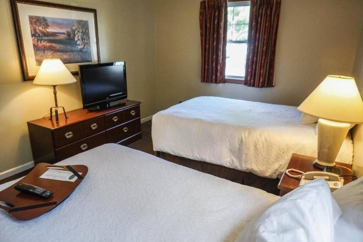 A hotel room with two beds, a TV on a dresser, lamps, and a window with curtains.