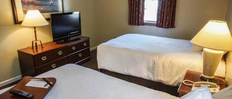 Una habitación de hotel con dos camas, un televisor en una cómoda, lámparas y un ventanal con cortinas.