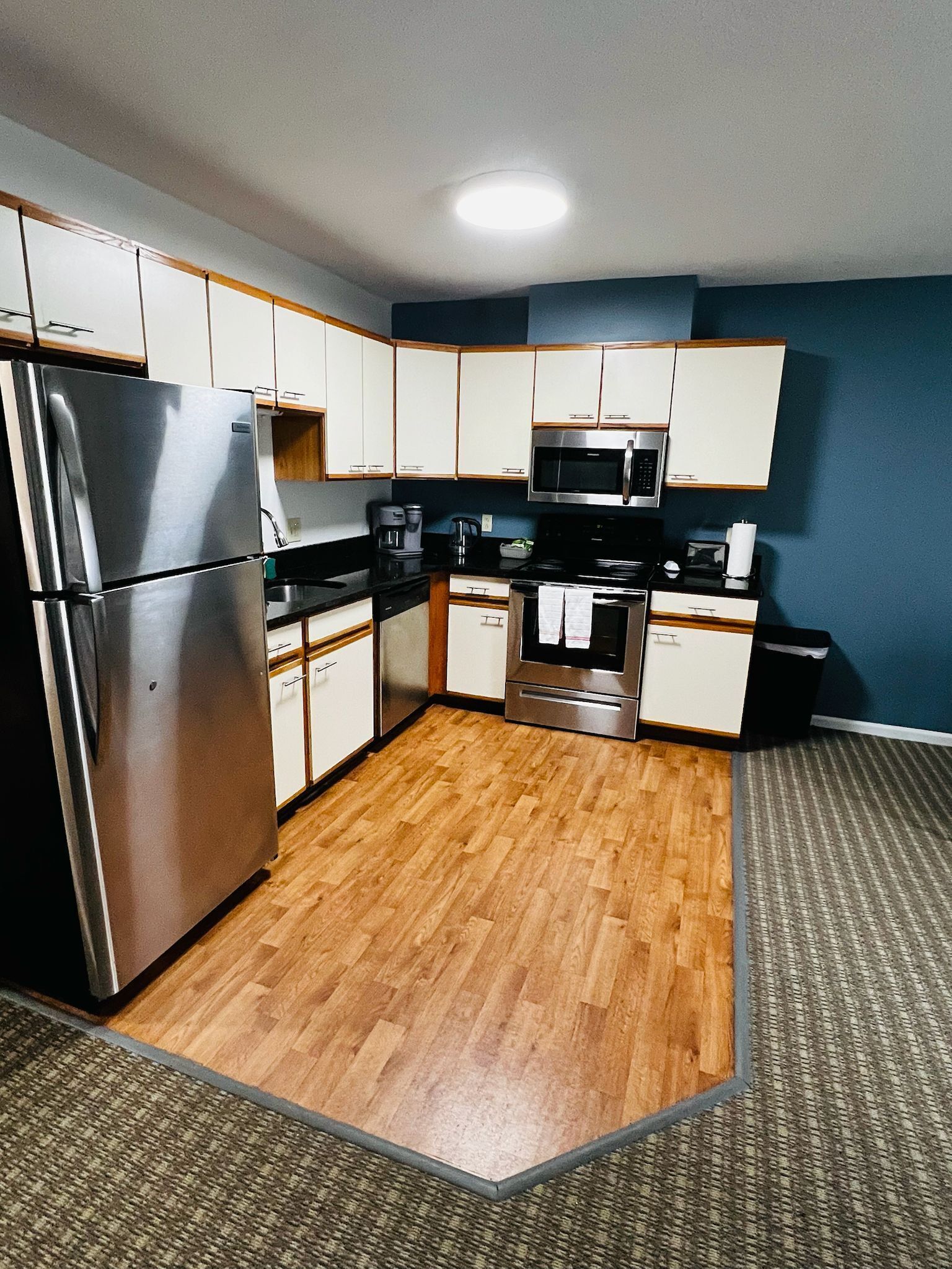 A compact kitchen with white cabinets, stainless steel appliances, and a herringbone-patterned floor.