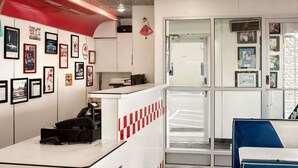 A retro-themed reception area with a checkered floor, a white counter with a phone, and various framed pictures on the walls.