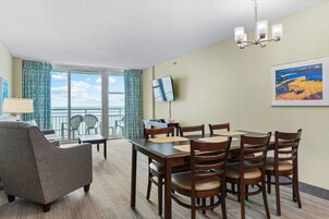 A hotel room with a dining area, a sofa, a TV, and a painting on the wall.