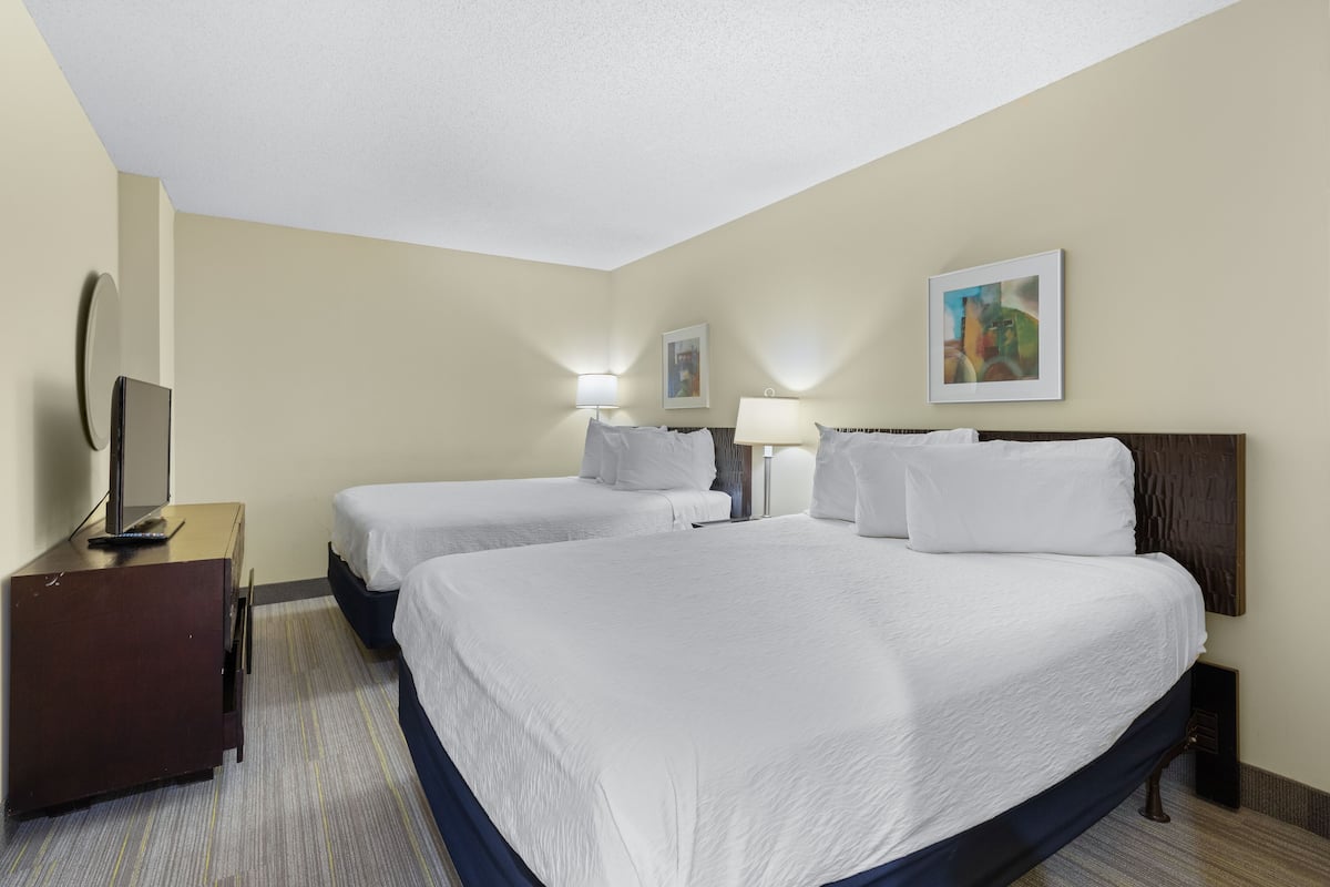 A hotel room with two beds, a desk with a TV, and two bedside lamps.
