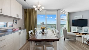 Una cocina moderna con una mesa de madera, sillas blancas y vistas de la ciudad a través de amplias ventanas.