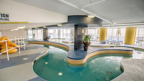 Una piscina interior con indicador de profundidad de 3 pies, sillas de descanso y vistas a la ciudad a través de amplias ventanas.