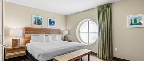 A hotel room with a large bed, a round window, a bench, and two bedside tables with lamps.