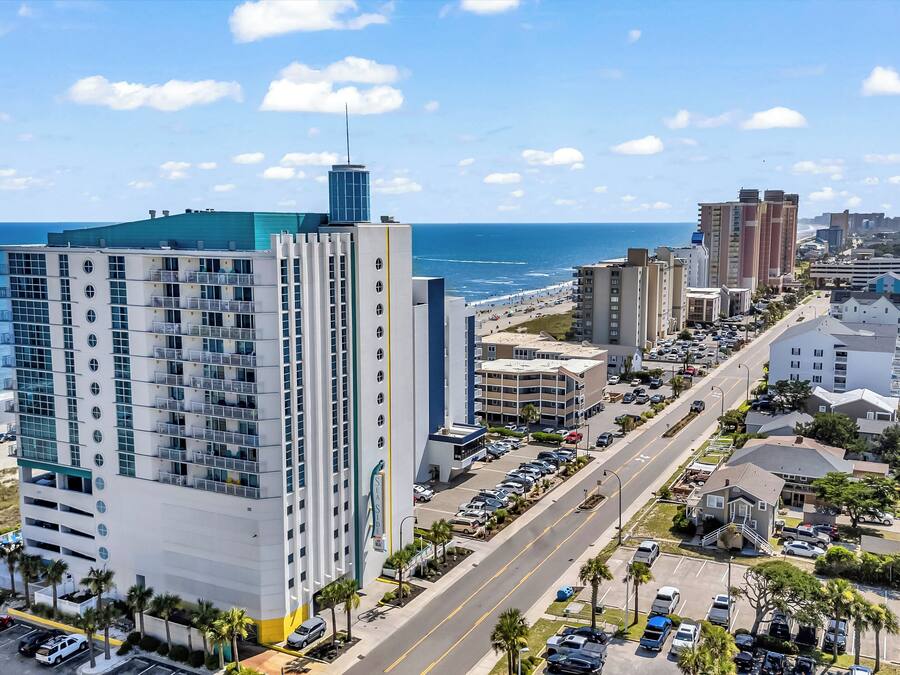 A high-rise hotel with multiple floors, a parking lot, and a beach view.