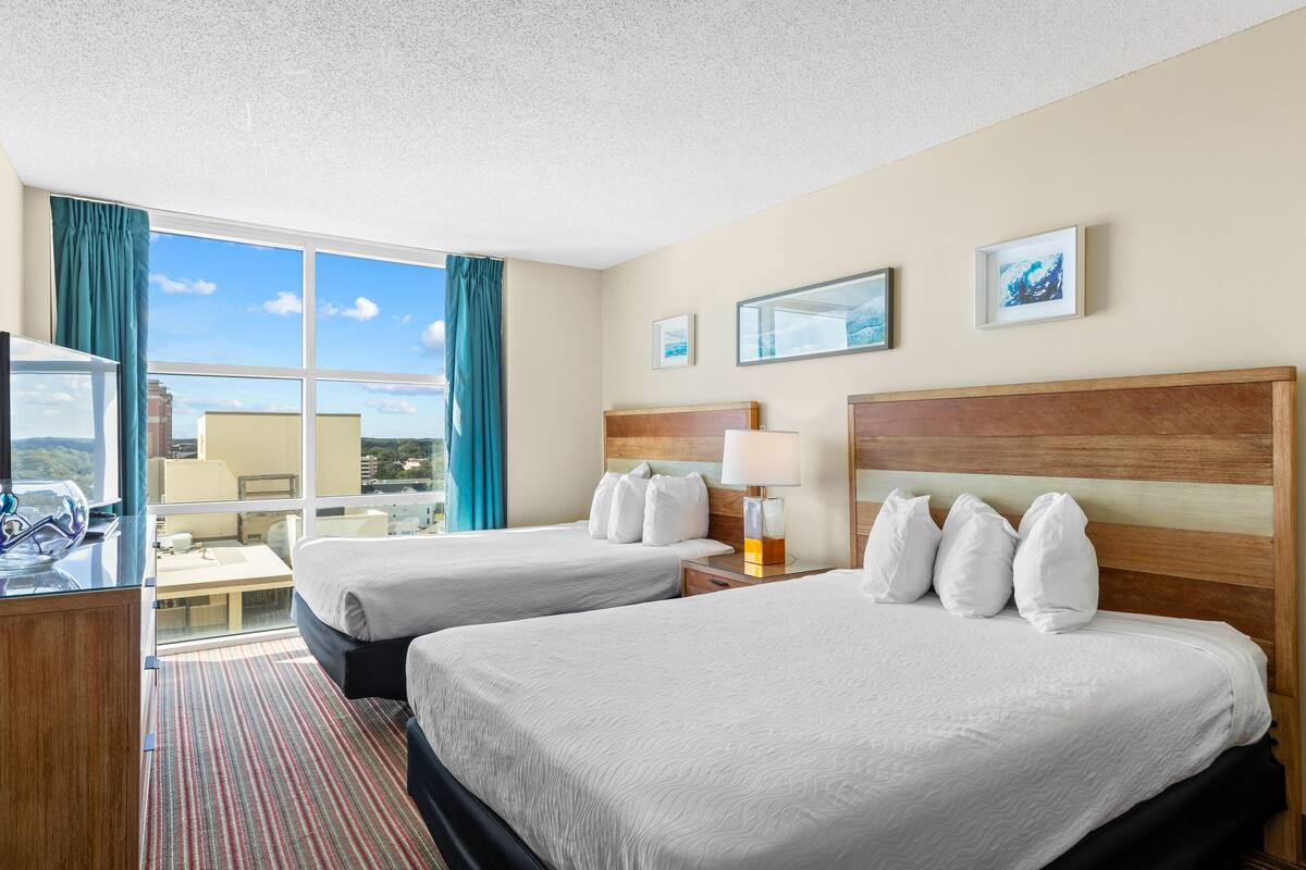 A hotel room with two beds, a desk, a chair, and a large window with curtains.