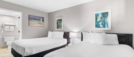 A hotel room with two beds, a bathroom, and artwork on the walls.