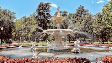 Una fuente de varios niveles con estatuas, rodeada por un jardín circular con follaje rojo.
