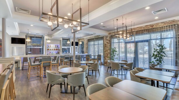 A modern restaurant with round tables and chairs, a bar area, and large windows with a view. - Staybridge Suites Savannah Historic District by IHG (Savannah)