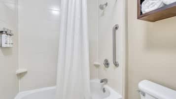 A bathroom with a white bathtub, a shower with a curtain, a toilet, and a shelf with towels.