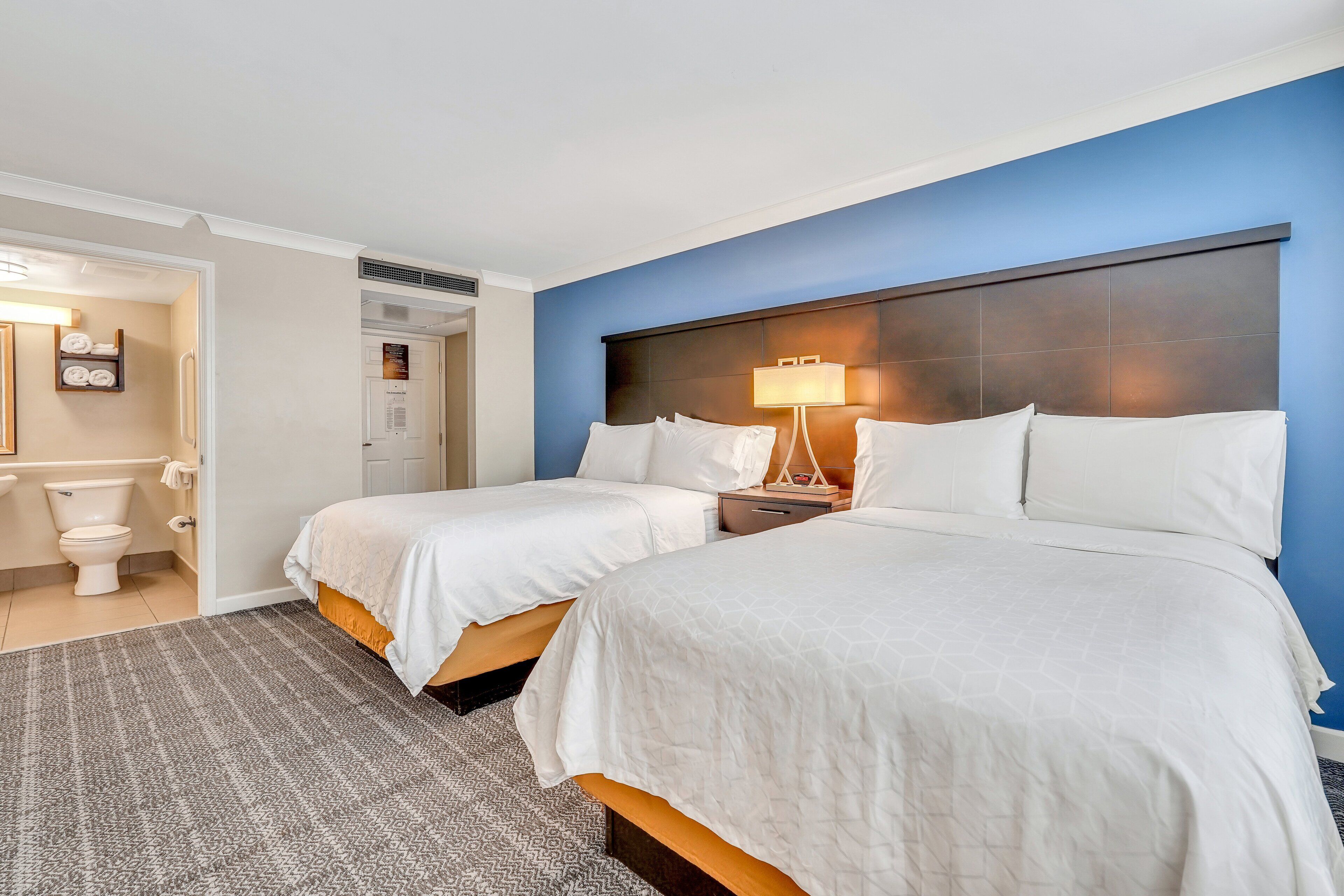 A hotel room with two beds, a bathroom, and a nightstand with a lamp.