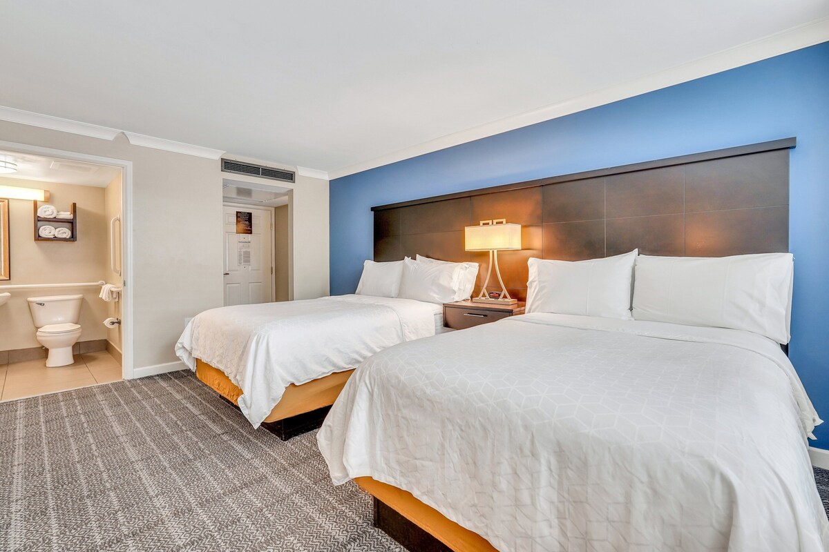 A hotel room with two beds, a bathroom, and a nightstand with a lamp.