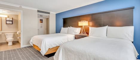 Une chambre d’hôtel avec deux lits, une salle de bain et une table de chevet avec une lampe.