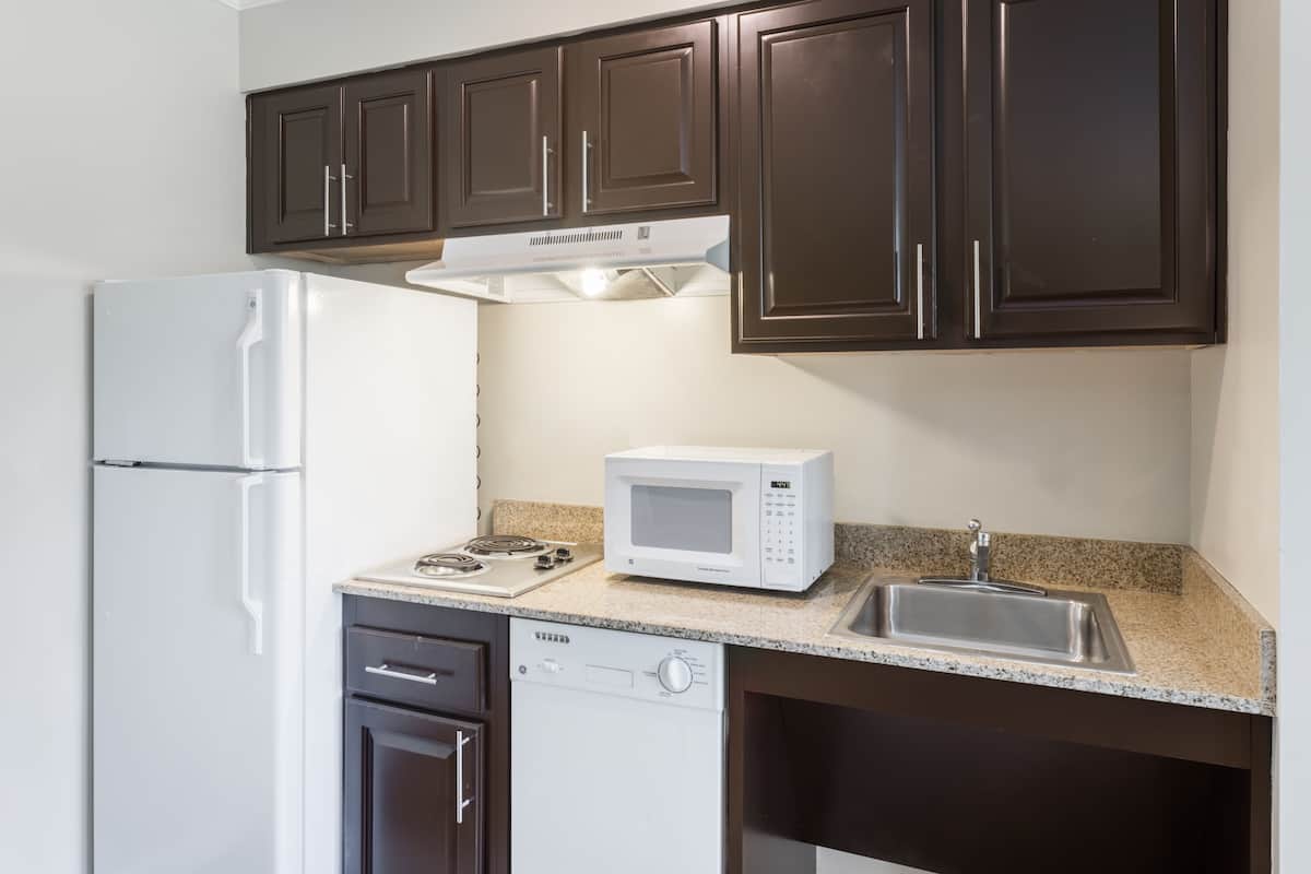 Una cocina con gabinetes marrón oscuro, un refrigerador blanco, un microondas, un lavavajillas y una encimera de granito.